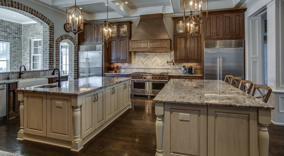 Huge arts and crafts u-shaped medium tone wood floor and brown floor enclosed kitchen photo with a farmhouse sink, raised-panel cabinets, medium tone wood cabinets, granite countertops, beige backsplash, mosaic tile backsplash, stainless steel appliances and two islands