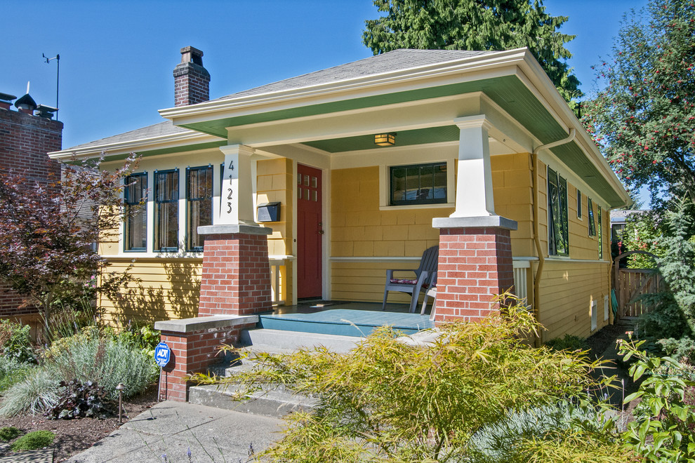 Photo of a small arts and crafts one-storey yellow house exterior in Seattle with wood siding, a gable roof and a shingle roof.