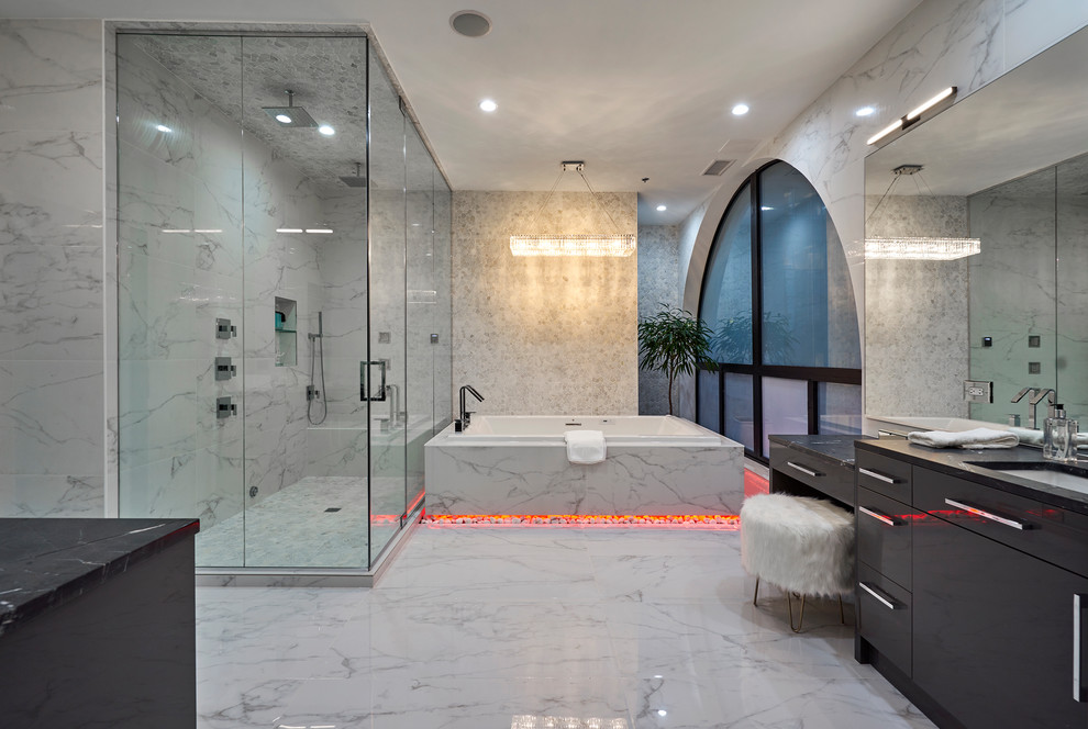 Photo of a contemporary master bathroom in Chicago with flat-panel cabinets, grey cabinets, a drop-in tub, a corner shower, gray tile, an undermount sink, white floor and black benchtops.
