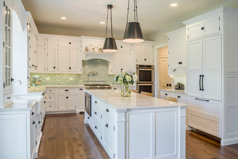 Photo of a large transitional u-shaped eat-in kitchen in Chicago with a farmhouse sink, glass-front cabinets, white cabinets, terrazzo benchtops, green splashback, glass tile splashback, medium hardwood floors, with island and stainless steel appliances.