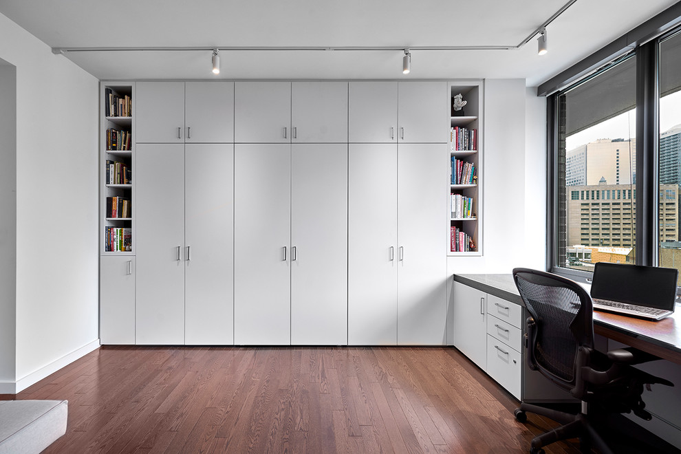 Photo of a large modern study room in Chicago with white walls, dark hardwood floors, no fireplace, a built-in desk and brown floor.