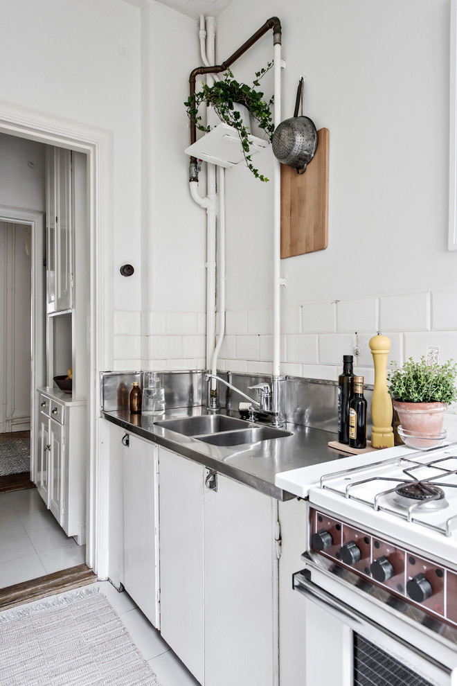 Scandinavian kitchen in Gothenburg with white cabinets and stainless steel benchtops.