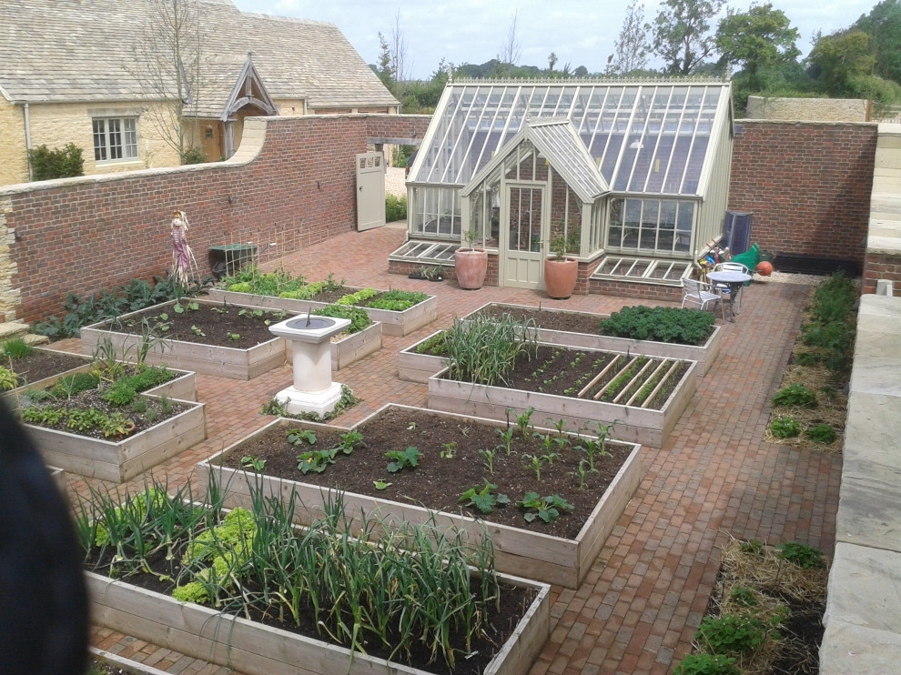 This is an example of a large backyard formal garden in Gloucestershire with with raised garden bed and river rock.