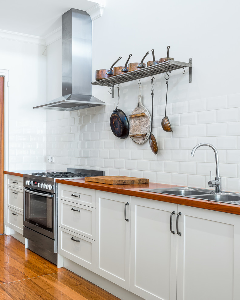 Inspiration for a mid-sized country galley eat-in kitchen in Sydney with a double-bowl sink, shaker cabinets, white cabinets, wood benchtops, white splashback, subway tile splashback, stainless steel appliances, medium hardwood floors, with island, brown floor and brown benchtop.