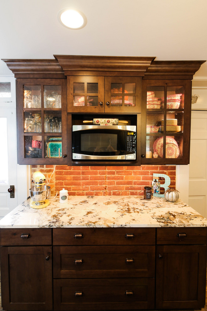 Example of a mid-sized mountain style l-shaped vinyl floor and brown floor enclosed kitchen design with a farmhouse sink, shaker cabinets, dark wood cabinets, granite countertops, white backsplash, ceramic backsplash, stainless steel appliances, an island and white countertops