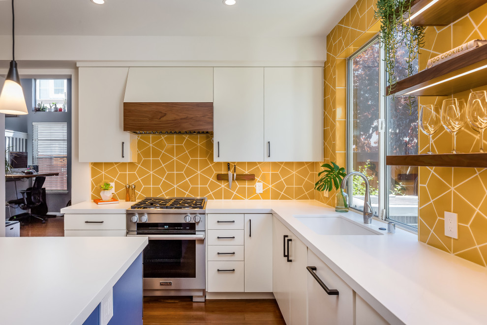 This is an example of a mid-sized midcentury u-shaped eat-in kitchen in San Francisco with an undermount sink, flat-panel cabinets, white cabinets, quartz benchtops, yellow splashback, ceramic splashback, stainless steel appliances, medium hardwood floors, with island, brown floor, white benchtop and timber.