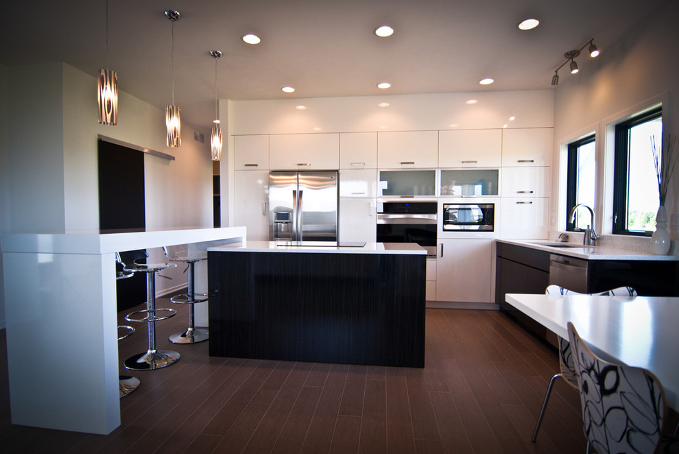 Photo of a small modern l-shaped eat-in kitchen in Grand Rapids with flat-panel cabinets, white cabinets, quartz benchtops, stainless steel appliances, dark hardwood floors, multiple islands, brown floor, white benchtop and an undermount sink.
