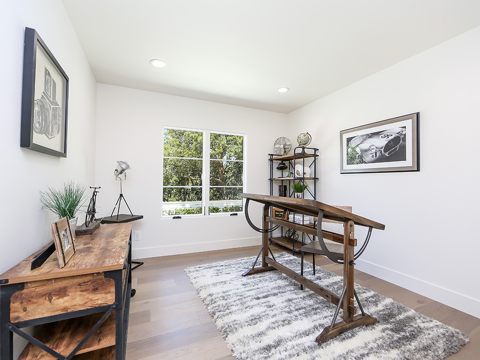 This is an example of a mid-sized industrial home studio in Los Angeles with white walls, dark hardwood floors, no fireplace and a freestanding desk.