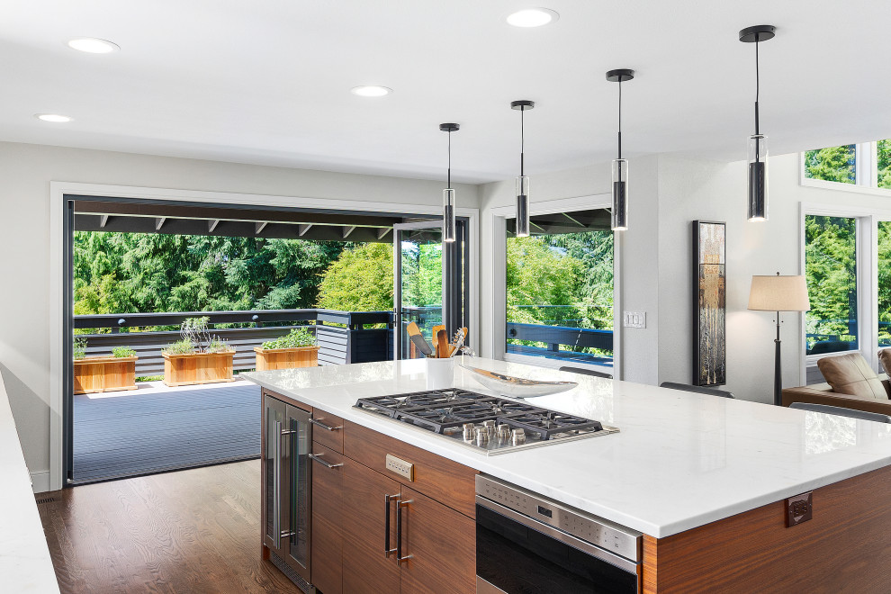 This is an example of a midcentury l-shaped kitchen in Seattle with a single-bowl sink, raised-panel cabinets, quartz benchtops, white splashback, engineered quartz splashback, stainless steel appliances, medium hardwood floors, with island and white benchtop.