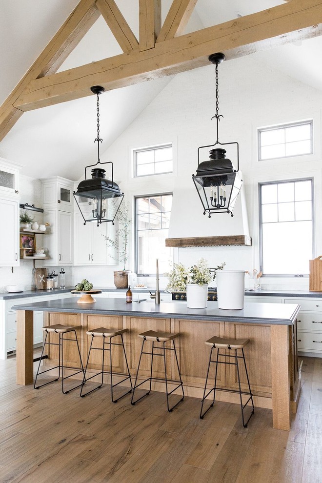 This is an example of a large country u-shaped kitchen in Salt Lake City with white cabinets, white splashback, black appliances, dark hardwood floors, with island, grey benchtop, shaker cabinets and brown floor.