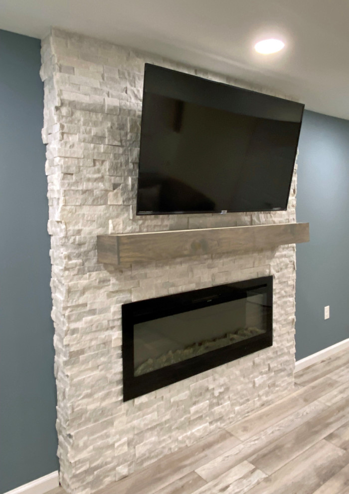 Idée de décoration pour un sous-sol design avec un mur gris, une cheminée standard et un manteau de cheminée en pierre.