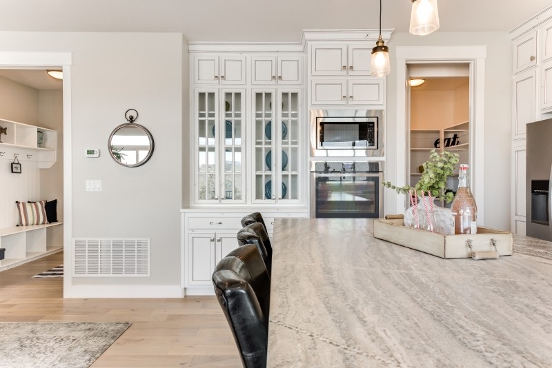 This is an example of a mid-sized beach style l-shaped open plan kitchen in Salt Lake City with a farmhouse sink, shaker cabinets, white cabinets, granite benchtops, beige splashback, ceramic splashback, stainless steel appliances, light hardwood floors and with island.