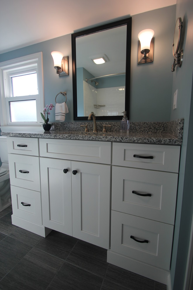 Photo of a mid-sized traditional bathroom in Cleveland with shaker cabinets, white cabinets, an alcove tub, a shower/bathtub combo, white tile, subway tile, blue walls, an undermount sink, granite benchtops, porcelain floors and grey floor.