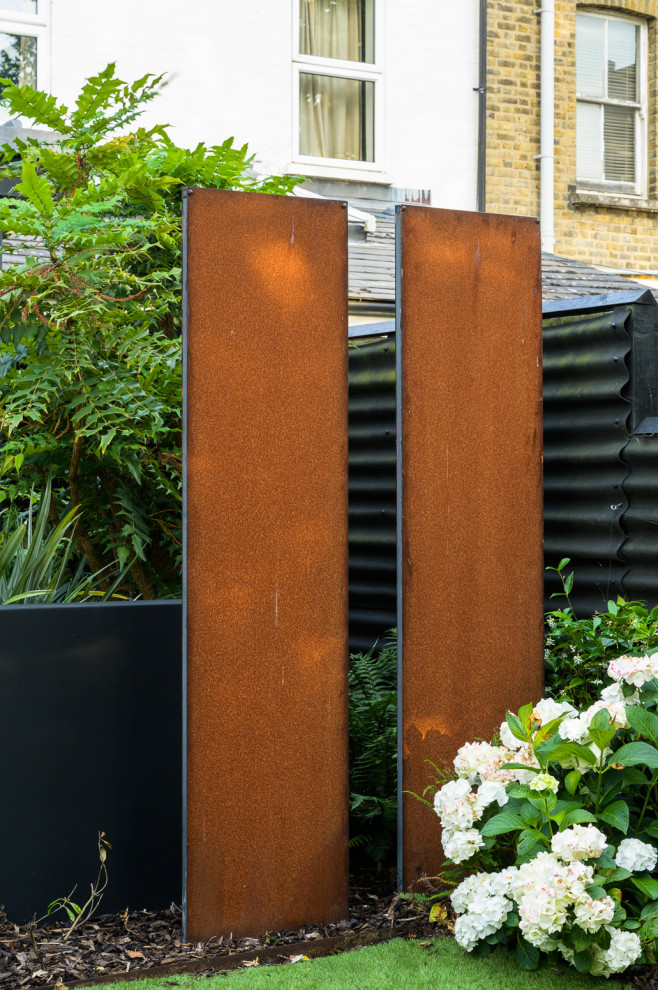 Photo of a mid-sized contemporary partial sun backyard stone and metal fence landscaping in London.