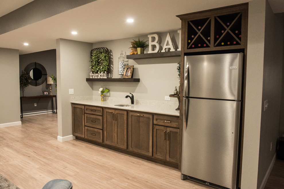 Example of a mid-sized mountain style single-wall light wood floor and brown floor wet bar design with an undermount sink, shaker cabinets, medium tone wood cabinets, quartz countertops, white backsplash and white countertops