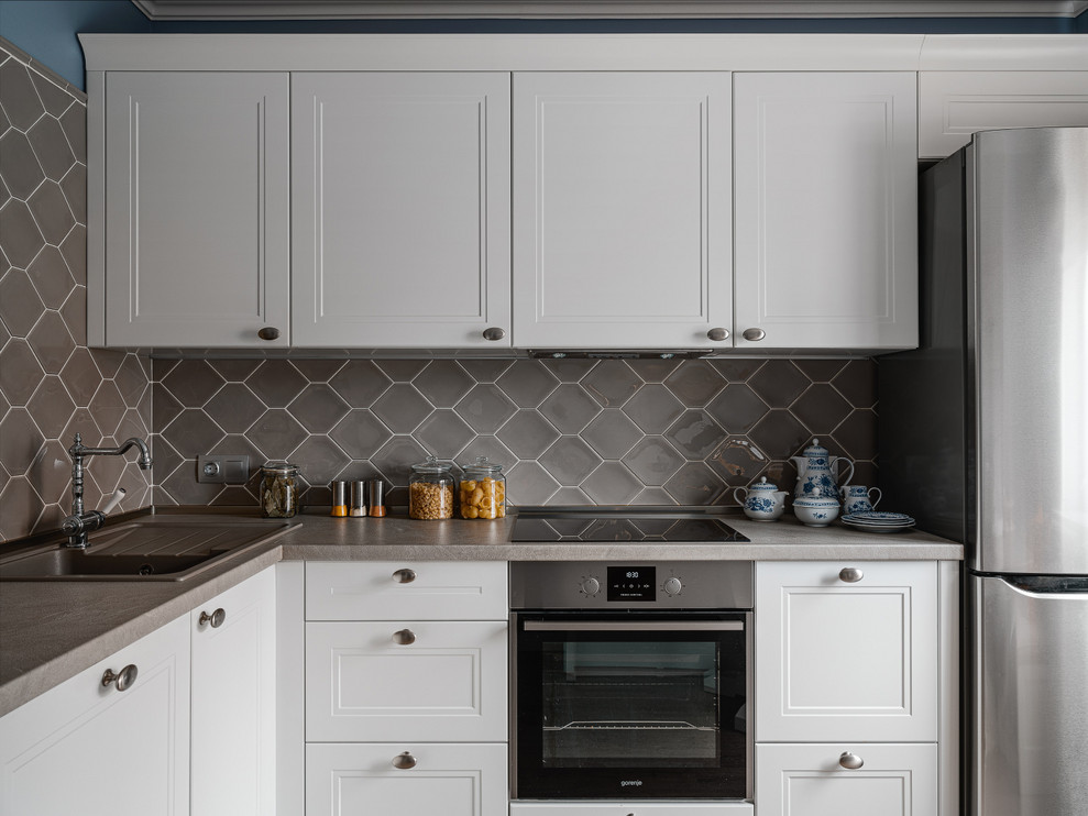 Small transitional l-shaped kitchen in Other with a drop-in sink, recessed-panel cabinets, white cabinets, grey splashback, grey benchtop and stainless steel appliances.