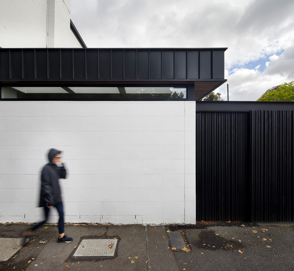 Photo of a small two-storey stucco white house exterior in Melbourne with a flat roof, a metal roof and a black roof.