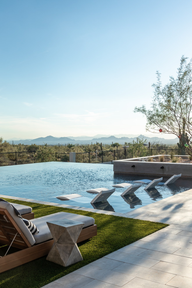 Large transitional backyard rectangular infinity pool in Phoenix with a hot tub and natural stone pavers.