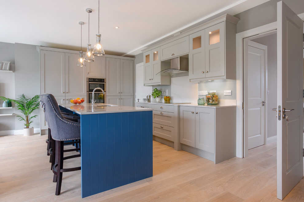 Large contemporary kitchen in Dublin with recessed-panel cabinets, grey cabinets, quartzite benchtops, white splashback, panelled appliances, light hardwood floors, with island and white benchtop.