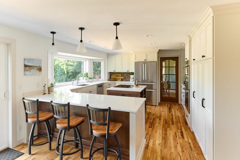 Mid-sized transitional u-shaped light wood floor and beige floor enclosed kitchen photo with an undermount sink, shaker cabinets, white cabinets, quartz countertops, red backsplash, brick backsplash, stainless steel appliances, a peninsula and white countertops