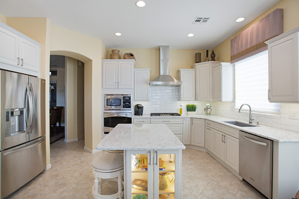 Example of a mid-sized transitional single-wall ceramic tile and beige floor eat-in kitchen design with an undermount sink, raised-panel cabinets, white cabinets, quartz countertops, white backsplash, porcelain backsplash, stainless steel appliances and an island