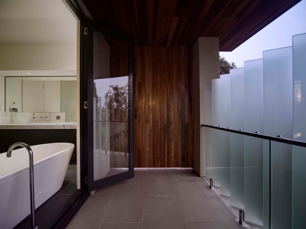 This is an example of a large contemporary master bathroom in Melbourne with flat-panel cabinets, black cabinets, a freestanding tub, an open shower, a wall-mount toilet, black and white tile, ceramic tile, white walls, ceramic floors, an undermount sink and marble benchtops.