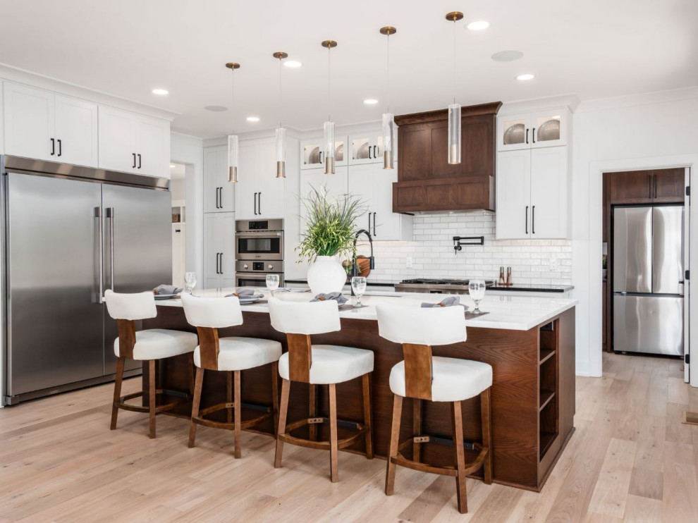 Example of a large transitional l-shaped light wood floor and brown floor eat-in kitchen design in Columbus with an undermount sink, flat-panel cabinets, dark wood cabinets, quartz countertops, white backsplash, ceramic backsplash, stainless steel appliances, an island and white countertops