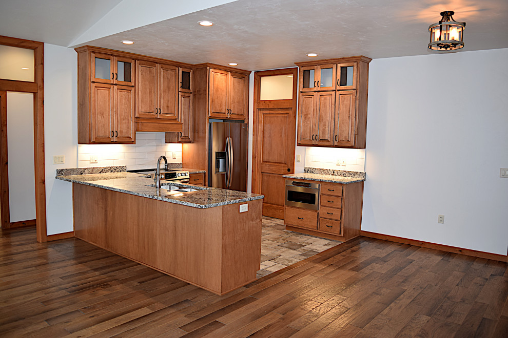 Mid-sized galley open concept kitchen photo with an undermount sink, raised-panel cabinets, granite countertops, ceramic backsplash, stainless steel appliances and a peninsula
