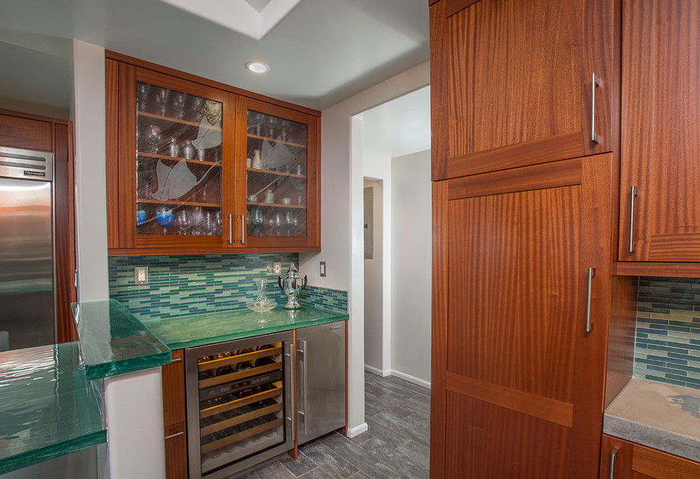 Photo of a small tropical wet bar in Hawaii with shaker cabinets, medium wood cabinets, glass benchtops, green splashback, glass tile splashback and porcelain floors.