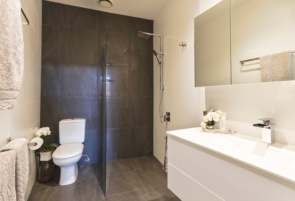 Design ideas for a mid-sized contemporary wet room bathroom in Brisbane with white cabinets, a two-piece toilet, white tile, porcelain tile, white walls, porcelain floors, an integrated sink and recycled glass benchtops.