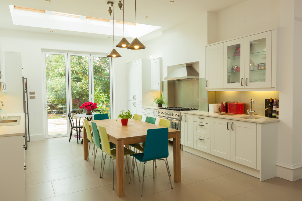 This is an example of a mid-sized contemporary galley eat-in kitchen in London with beige floor, beige cabinets, glass sheet splashback and stainless steel appliances.