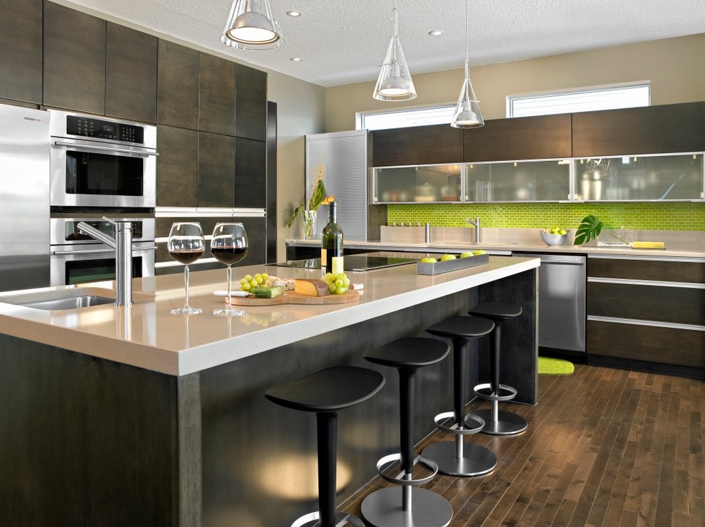 This is an example of a large contemporary kitchen in Edmonton with a drop-in sink, flat-panel cabinets, brown cabinets, quartzite benchtops, green splashback, glass tile splashback, stainless steel appliances, medium hardwood floors and with island.
