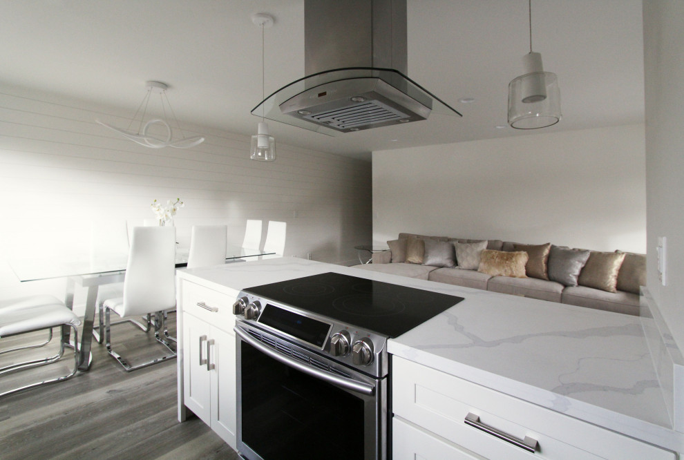 Open concept kitchen - small galley vinyl floor and brown floor open concept kitchen idea with an undermount sink, shaker cabinets, white cabinets, quartz countertops, white backsplash, quartz backsplash, stainless steel appliances, a peninsula and white countertops