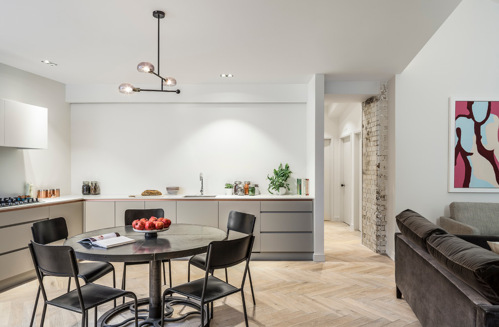 This is an example of a mid-sized contemporary eat-in kitchen in London with grey cabinets, stainless steel appliances and light hardwood floors.