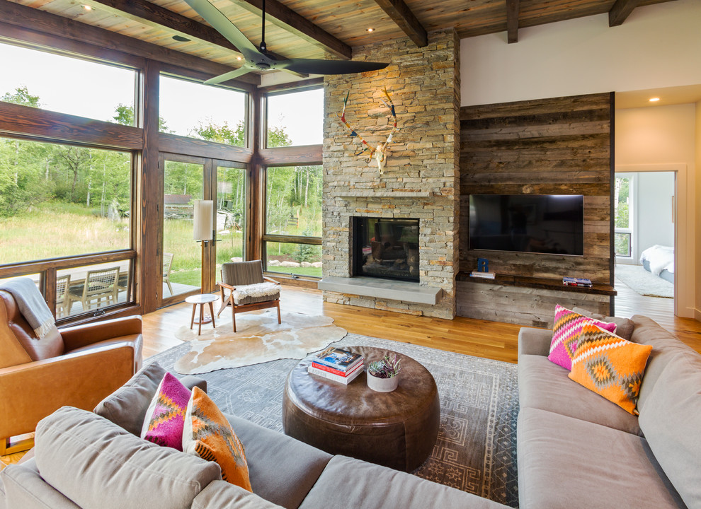 Design ideas for a country family room in Denver with white walls, medium hardwood floors, a standard fireplace, a stone fireplace surround, a wall-mounted tv and brown floor.