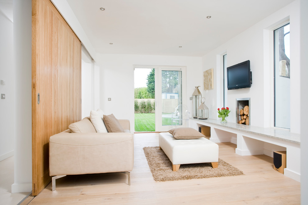 This is an example of a mid-sized contemporary open concept living room in Dublin with white walls, light hardwood floors, a standard fireplace, a plaster fireplace surround and a wall-mounted tv.