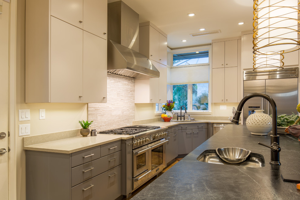 This is an example of a large modern l-shaped eat-in kitchen in Austin with an undermount sink, flat-panel cabinets, grey cabinets, soapstone benchtops, beige splashback, matchstick tile splashback, stainless steel appliances, light hardwood floors and with island.