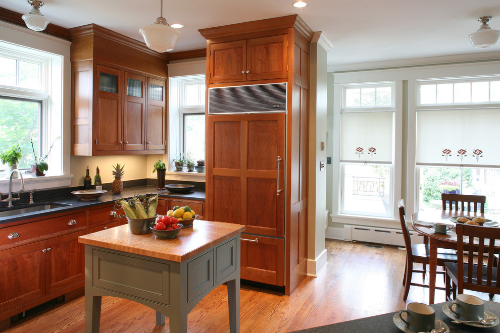 This is an example of a mid-sized arts and crafts u-shaped eat-in kitchen in DC Metro with an undermount sink, recessed-panel cabinets, medium wood cabinets, wood benchtops, beige splashback, stone slab splashback, stainless steel appliances, light hardwood floors, with island and red floor.