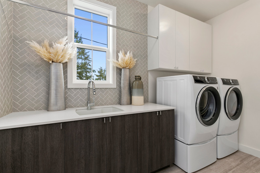 Example of a large farmhouse galley ceramic tile and beige floor dedicated laundry room design in Seattle with an undermount sink, flat-panel cabinets, dark wood cabinets, quartz countertops, gray backsplash, glass tile backsplash, white walls, a side-by-side washer/dryer and white countertops