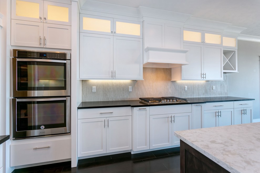 Example of a large transitional l-shaped dark wood floor open concept kitchen design in Seattle with an undermount sink, shaker cabinets, white cabinets, quartz countertops, gray backsplash, porcelain backsplash, stainless steel appliances, an island and white countertops