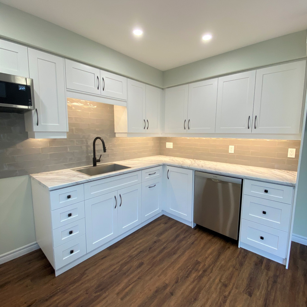 Example of a mid-sized transitional galley vinyl floor eat-in kitchen design in Toronto with a drop-in sink, shaker cabinets, white cabinets, laminate countertops, gray backsplash and stainless steel appliances