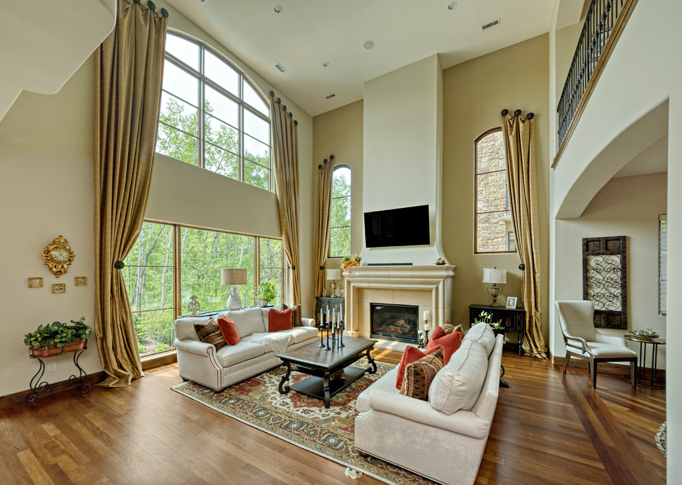 Photo of a large mediterranean loft-style living room in Minneapolis with beige walls, medium hardwood floors, a standard fireplace, a stone fireplace surround, a wall-mounted tv and brown floor.