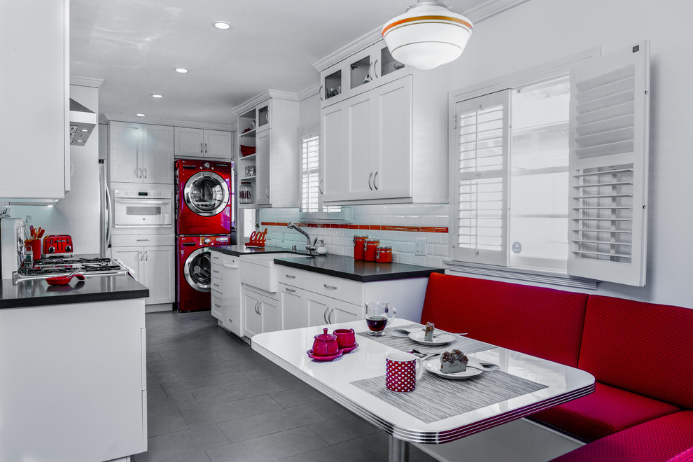 Photo of a mid-sized transitional galley separate kitchen in Los Angeles with a farmhouse sink, shaker cabinets, white cabinets, white splashback, subway tile splashback, white appliances and porcelain floors.
