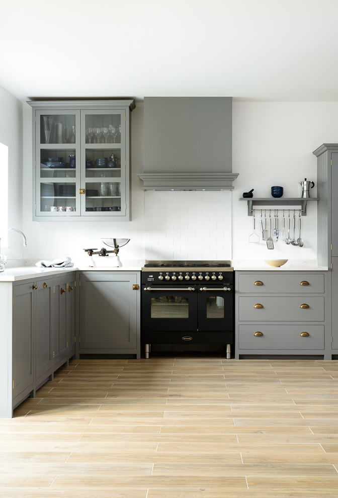 Photo of a mid-sized transitional l-shaped eat-in kitchen in Other with an integrated sink, shaker cabinets, grey cabinets, solid surface benchtops, white splashback, subway tile splashback, black appliances, porcelain floors and no island.