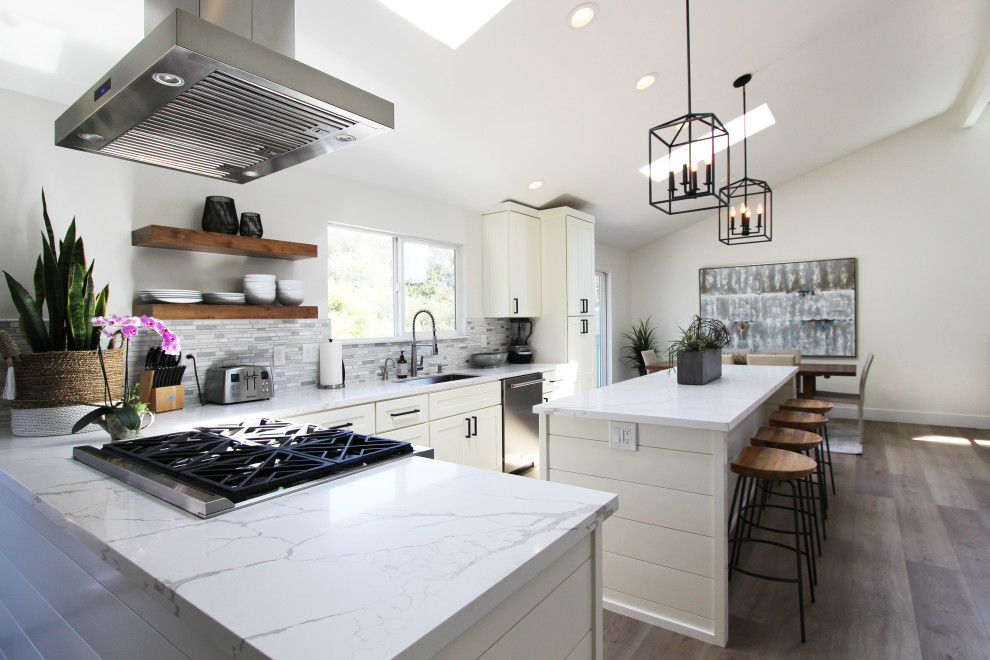 Mid-sized transitional l-shaped vinyl floor, brown floor and vaulted ceiling eat-in kitchen photo with an undermount sink, shaker cabinets, white cabinets, quartz countertops, multicolored backsplash, mosaic tile backsplash, stainless steel appliances, an island and white countertops
