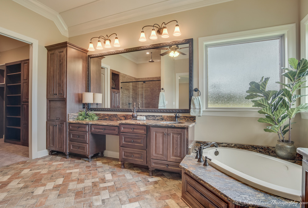 Inspiration for a large country master bathroom in New Orleans with raised-panel cabinets, medium wood cabinets, granite benchtops, a corner tub, stone tile, an alcove shower, an undermount sink, a two-piece toilet, beige walls and brick floors.