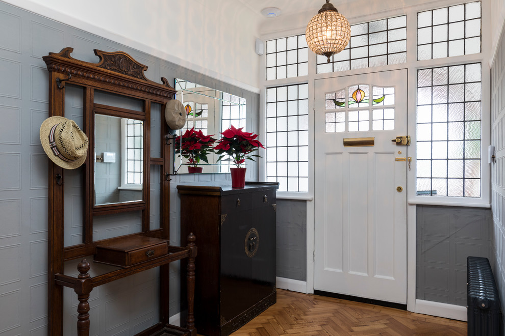 This is an example of a traditional foyer in London with multi-coloured walls, medium hardwood floors, a single front door and a white front door.