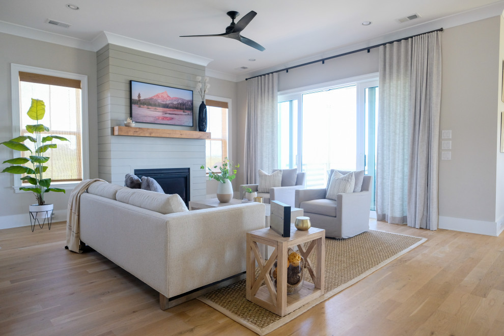 This is an example of a mid-sized beach style open concept living room in Charleston with grey walls, medium hardwood floors, a standard fireplace and a wall-mounted tv.