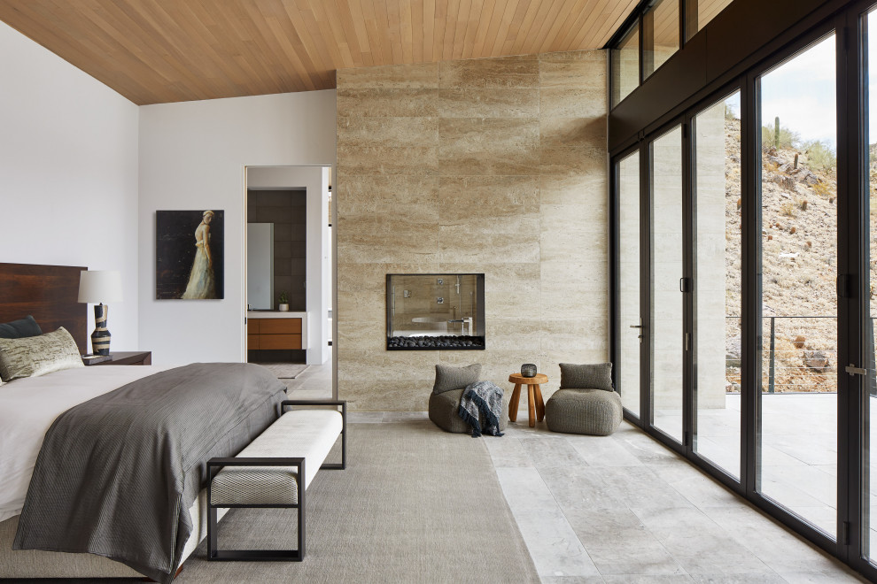 Свежая идея для дизайна: огромная хозяйская спальня в стиле модернизм с белыми стенами, полом из известняка, двусторонним камином, фасадом камина из камня и деревянным потолком - отличное фото интерьера
