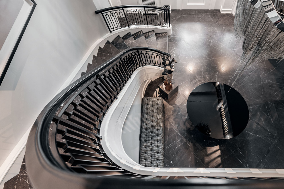 На фото: большая изогнутая лестница в классическом стиле с мраморными ступенями, подступенками из мрамора и металлическими перилами с